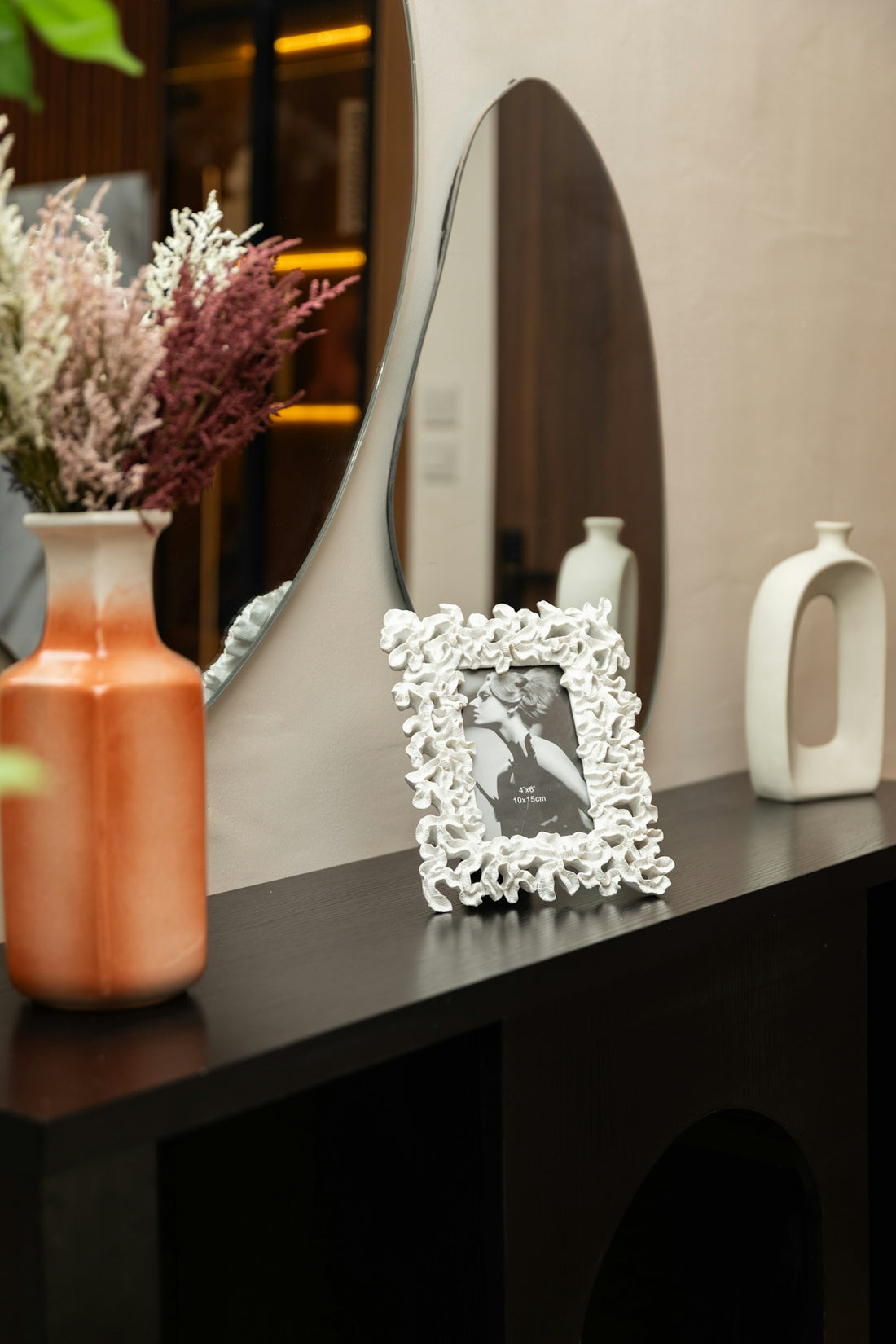Black console table with vase, photo frame, and decorative mirror